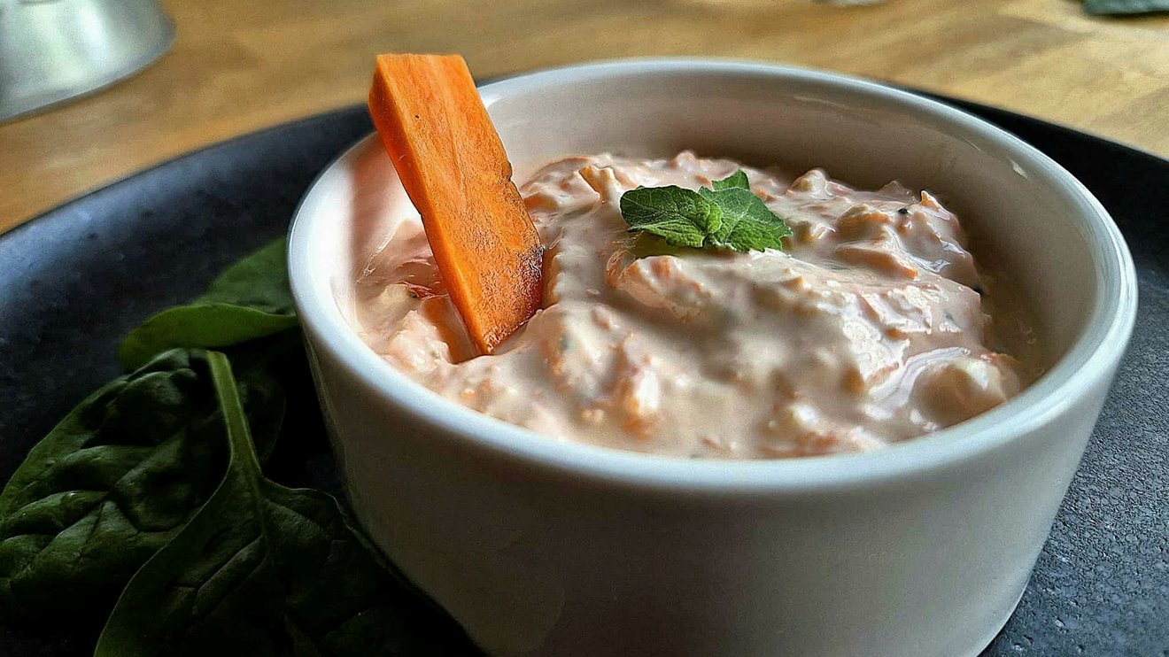 En vit skål med morotstzatziki med en morotsstav som sticker upp