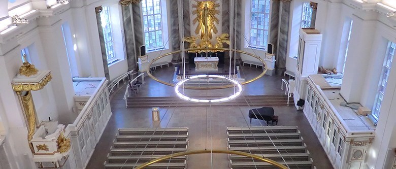 Vi blickar ned i kyrksalen i Gustavi Domkyrka. Till vänster syns predikstolen och längst fram altaret. Inredningen går i vitt och guld.