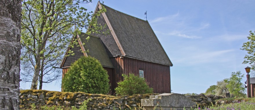 Hedareds stavkyrka. Kyrkan är i brunt trä och mörkare tak.