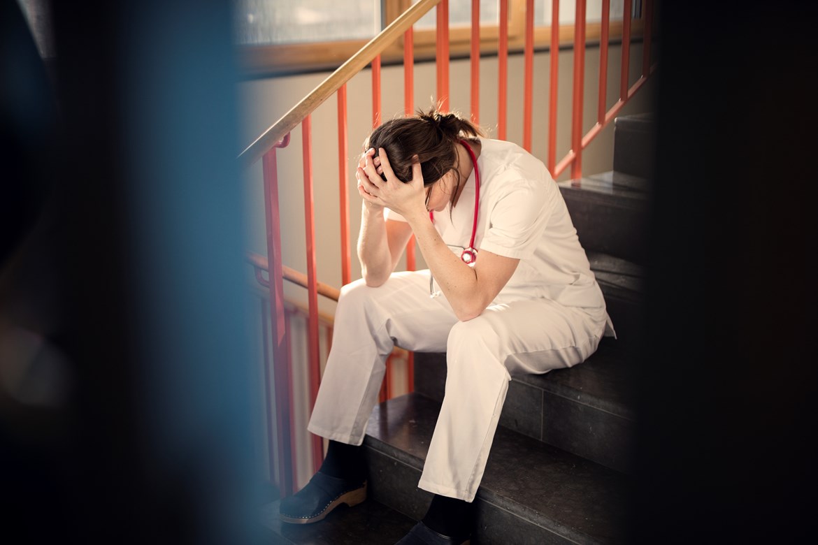 Kvinna som arbetar i vården sitter utmattad i en trappa