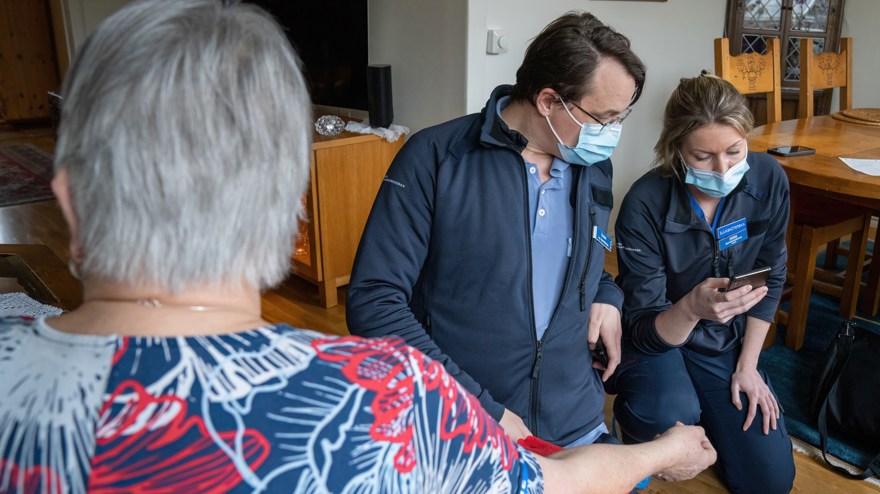Två vårdare avläser data på mobil hos en kvinnlig patient i hemmet