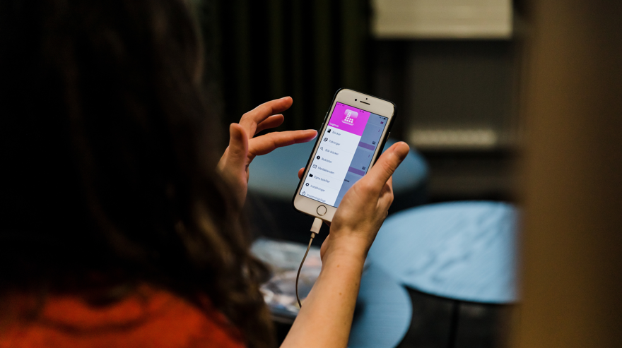 Två händer håller i en telefon, skärmen visar menyn i Legimus app.