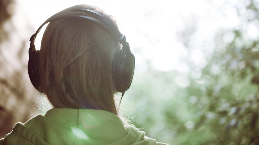 Kvinna bakifrån med hörlurar lyssnar på talbok