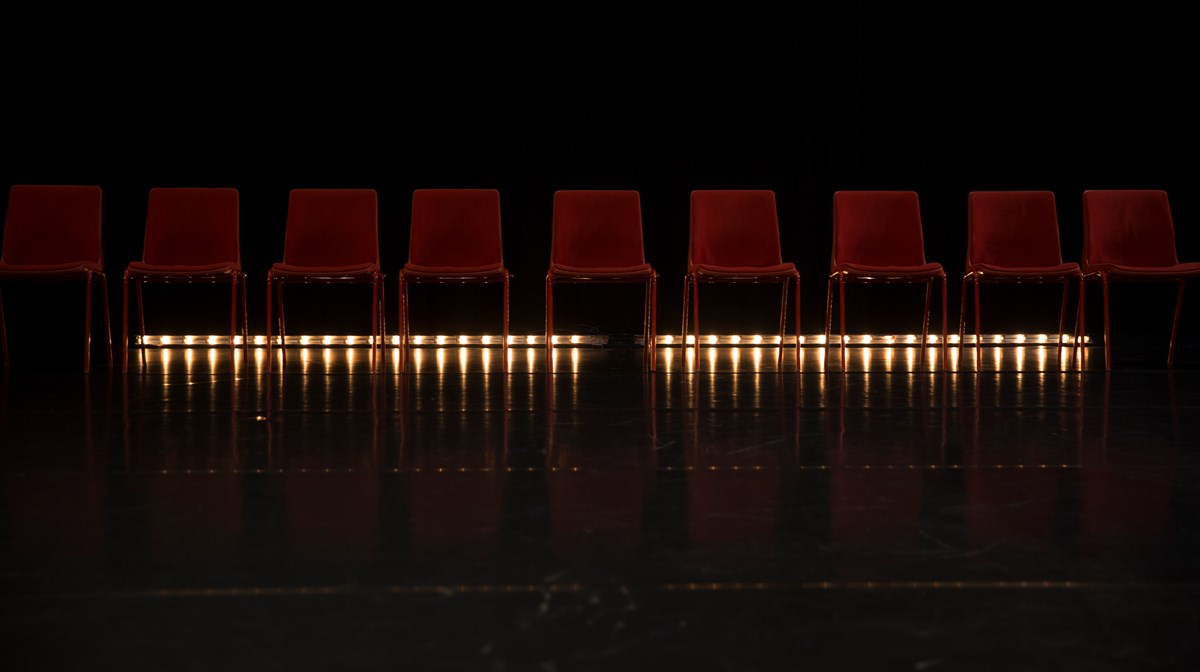 En rad röda stolar på en scen med belysning underifrån.