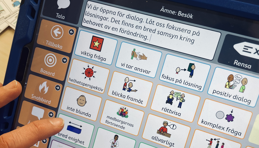 En hand pekar på en kommunikationsanpassning i ett hjälpmedel. Det finns fraser som passar för en minister.