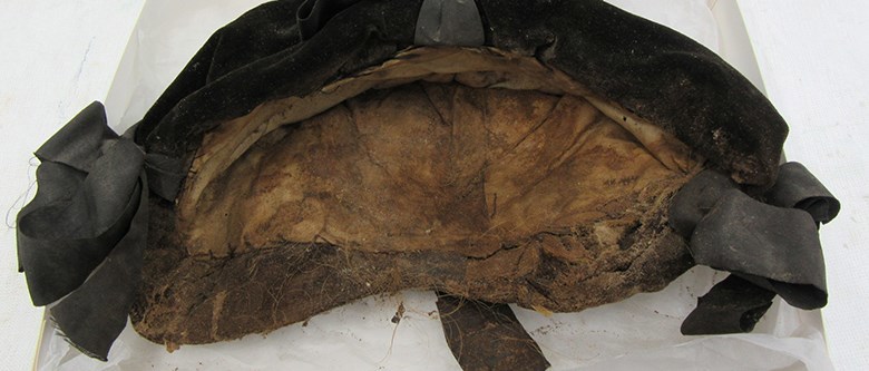 En brunaktig sammetsmössa med hårrester i ligger på vitt silkepapper.