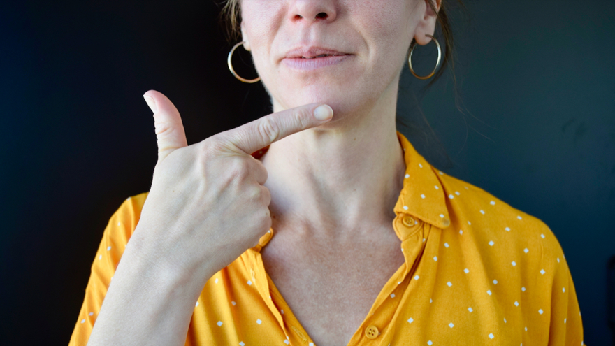 En kvinna i gul blus teckenspråktecknet för ordet "tack".