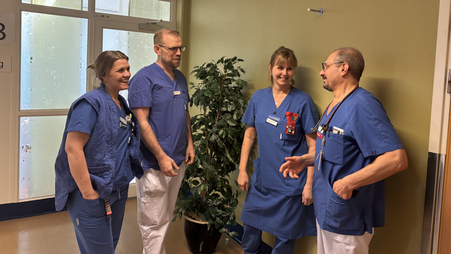 Fyra blåklädda läkare och sjuksköterskor står och pratar i en sjukhuskorridor.