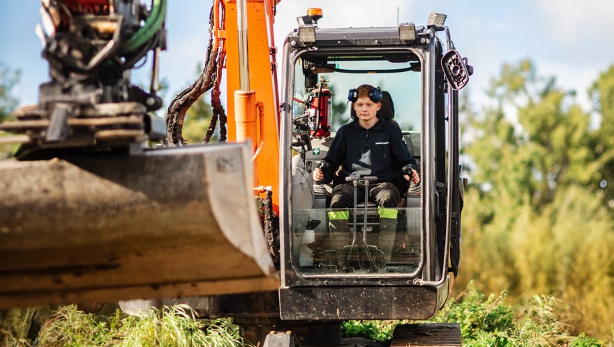 Elev sitter i grävmaskin med skopan i förgrunden