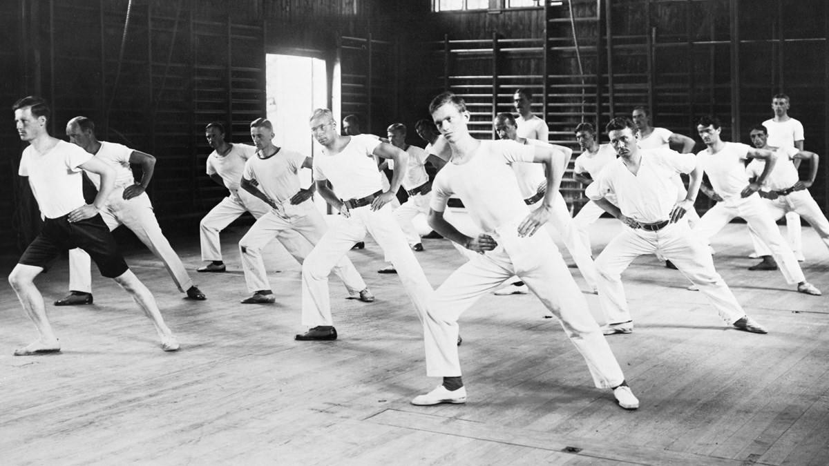 En grupp män gymnastiserar i en gymnastikhall på tidigt 1900-tal