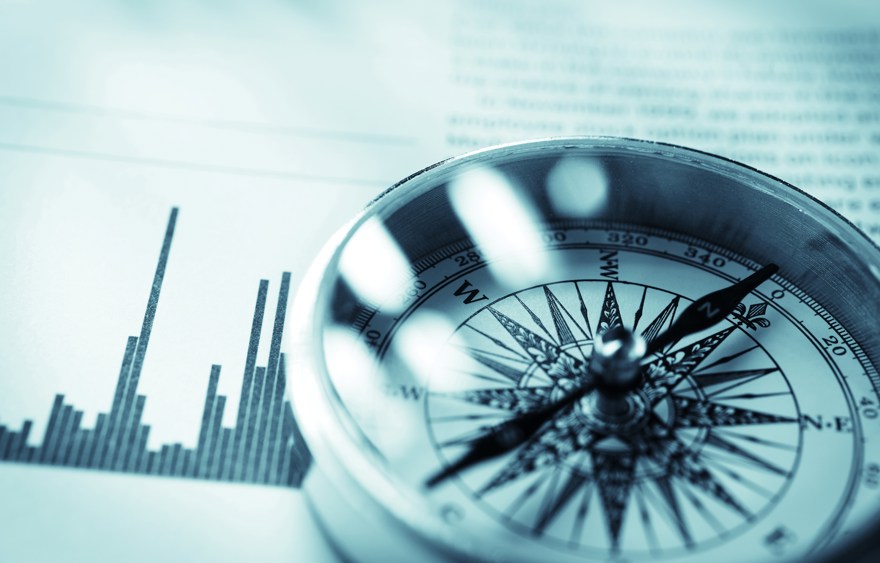 Close-up of a compass on stock market data chart.