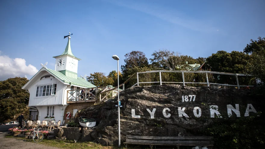 Ett vitt sekelskiftshus med ett klocktorn bredvid en veranda som är byggd på en klippa.