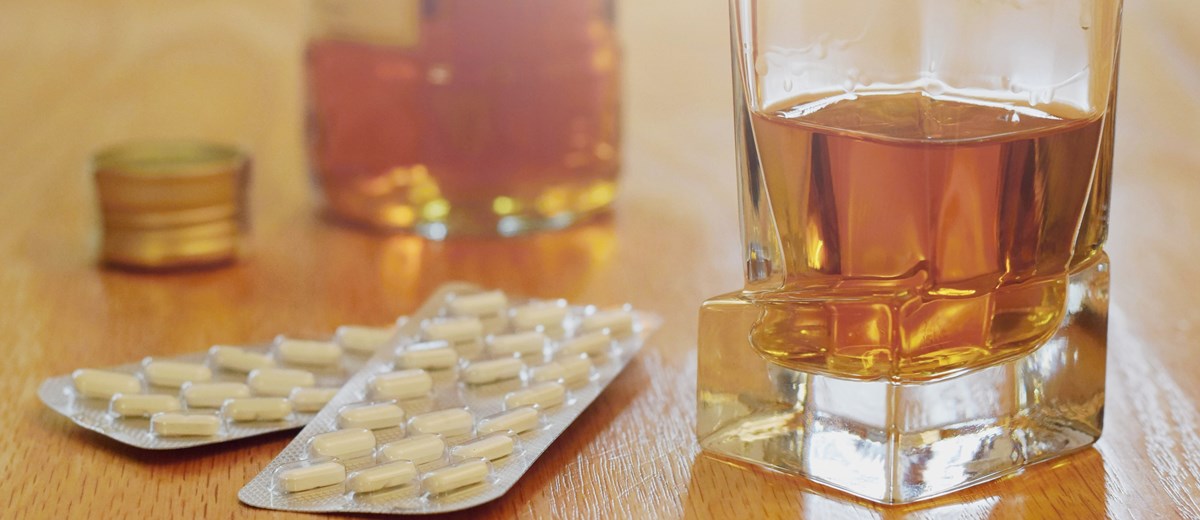 Bilden visar en närbild av ett glas med wiskey och två kartor med tabletter på ett bord.