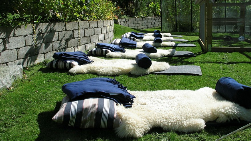 Liggunderlag, fårfällar och kuddar på gräsmatta i Gröna Rehabs trädgård. Snart börjar övning i kroppskännedom