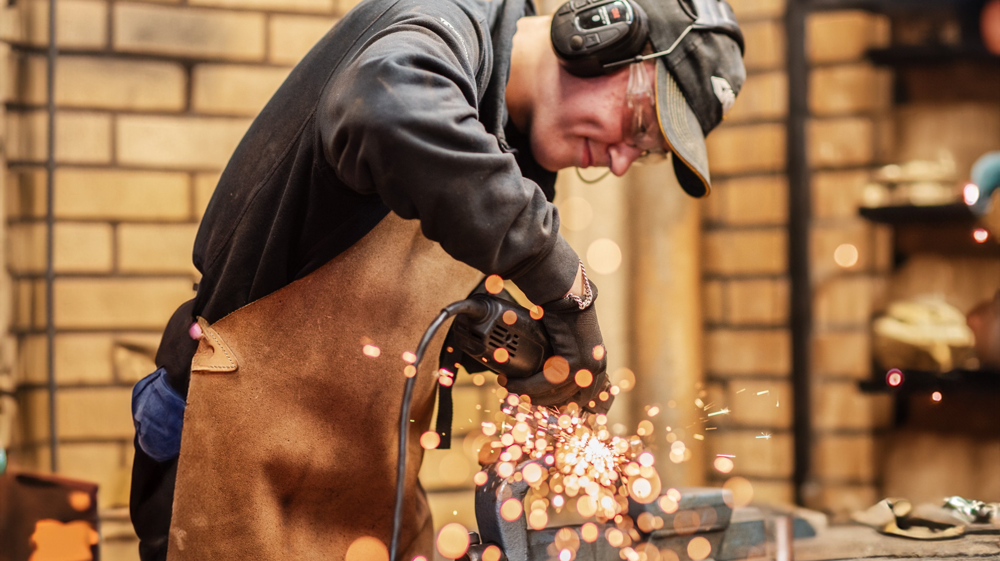 Gnistor slår upp framför elev med hörselskydd och skyddskläder som använder en slipmaskin i verkstadsmiljö