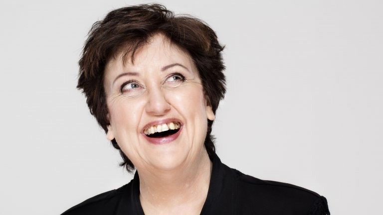 Babben Larsson har kortklippt brunt hår. Hon är klädd i en svart skjorta och hon ler stort.