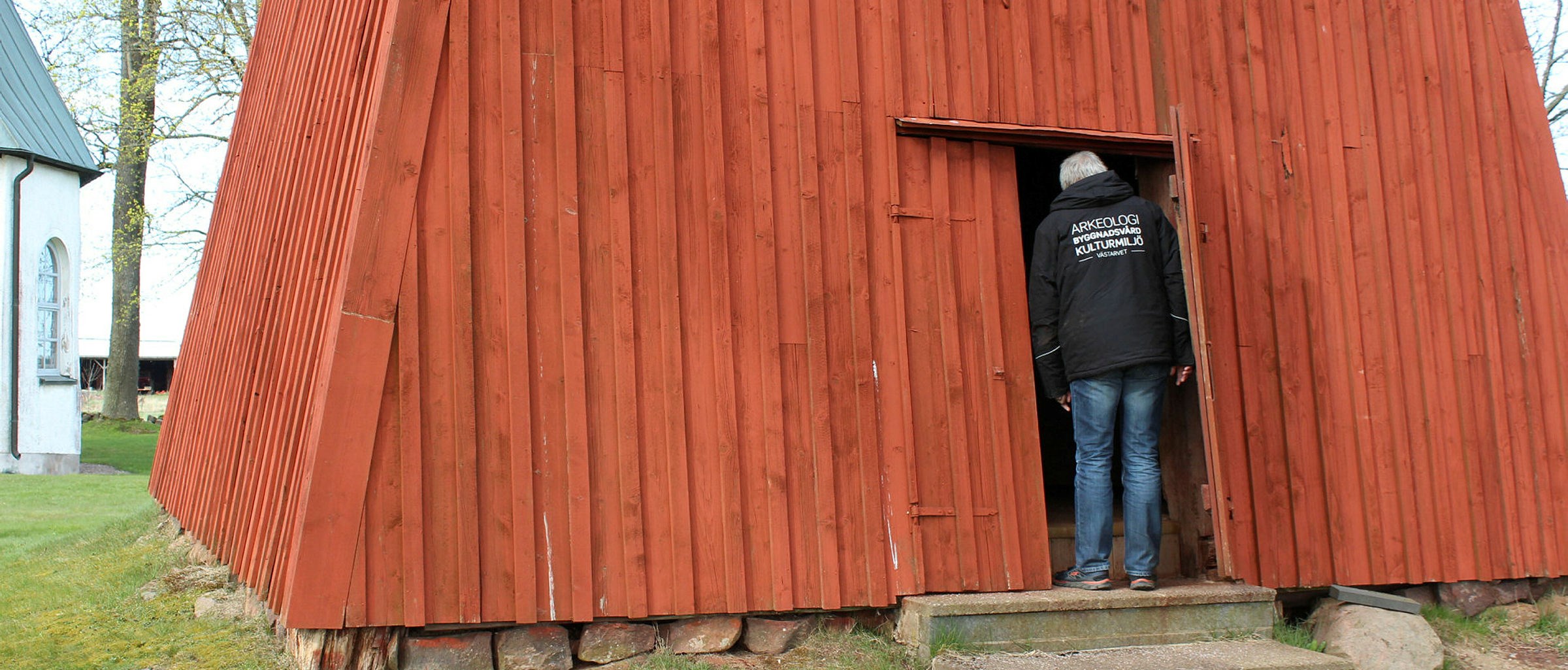 Person som tittar in i rödmålad byggnad, klocktorn. 