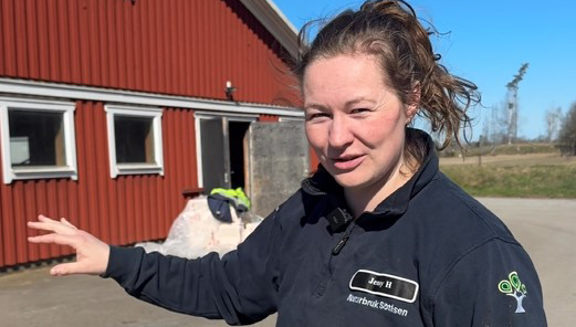 Jenny står vida ladugården och visar vart mjölkroboten ska byggas