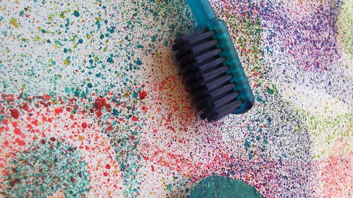 Olika färger är stänkt i olika mönster. En tandborste ligger på målningen.