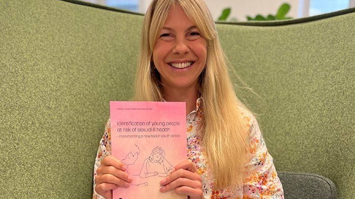 Sofia Hammarström sitter i en soffa och håller sin publikation framför sig. Hon ler och ser glad ut.