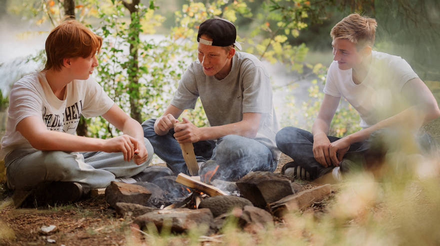 Tre elever sitter tillsammans vid en brasa i skogen