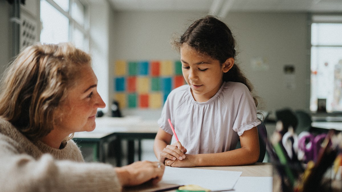 En lärare pratar med en tioårig elev i ett klassrum