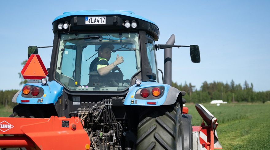Elev sitter i hytten på en traktor och gör tummen upp