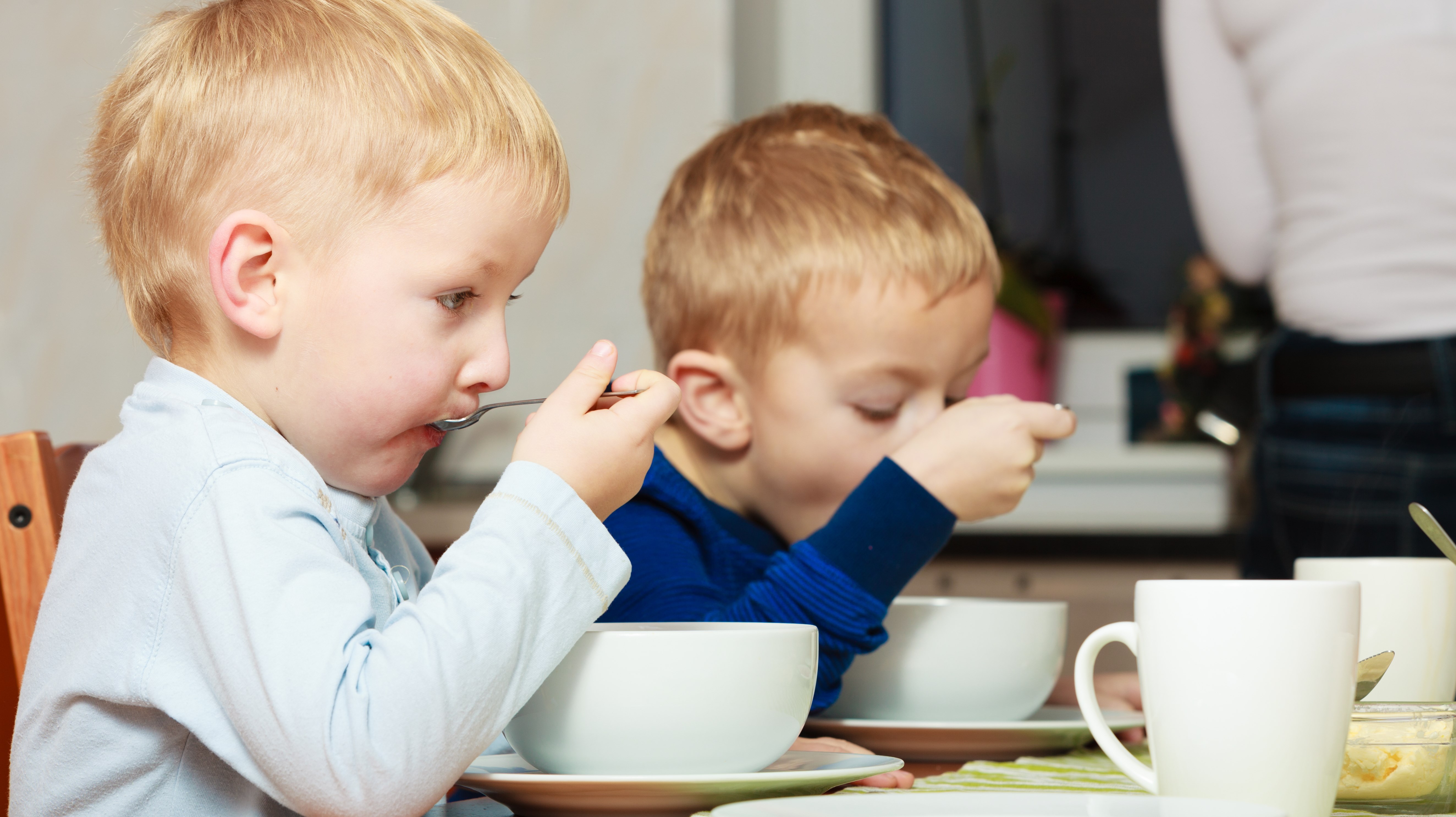 Två små barn äter frukost i djupa skålar