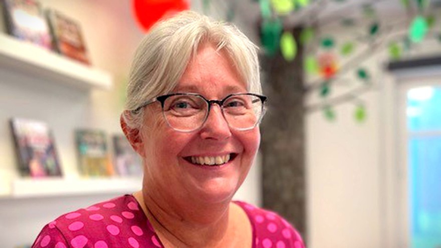 Camilla Oscarsson är i medelåldern och har långt grått hår som är uppsatt. Hon bär glasögon och är klädd i en rosaprickig tröja. Bakom henne syns böcker på en vägg, hon ler mot kameran.