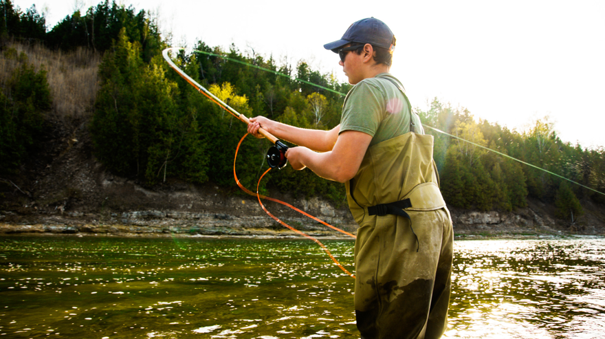 Kille med keps flugfiskar i vattendrag