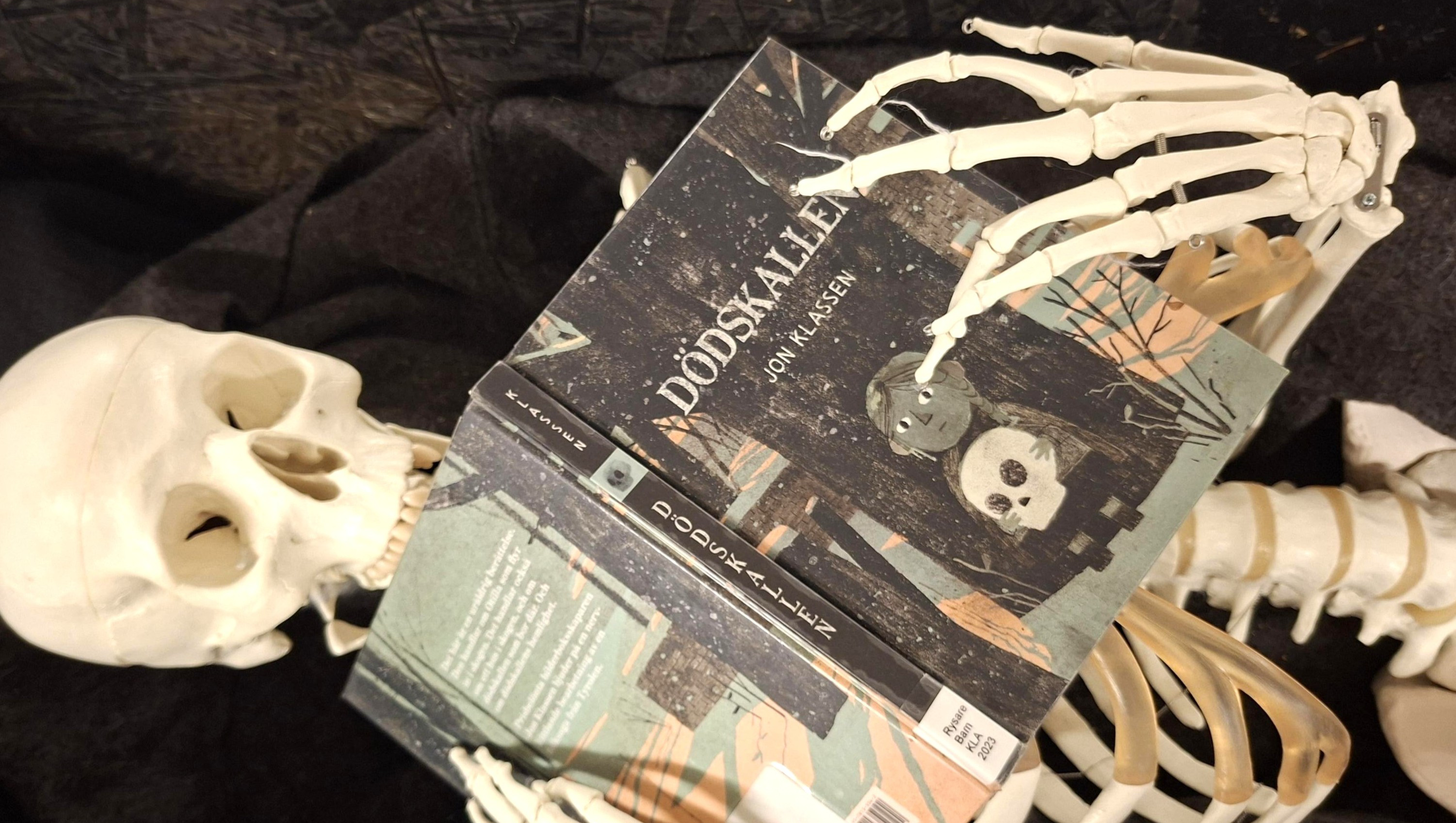 Ett skelett håller i en bok med titeln Dödskallen.
