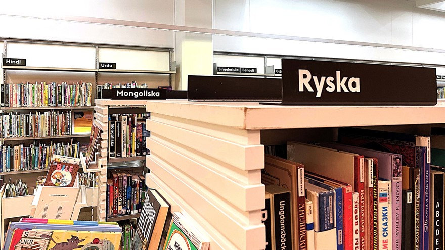 I förgrunden finns en skylt längst upp på en bokhylla, det står Ryska på skylten. Längre bort i rummet finns fler fyllda bokhyllor med olika skyltar: Urdu, Mongoliska, Hindi osv