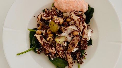 Quinoa på en bädd av spenat toppat med kikärtor och kyckling. En rosa sås på tallrikens sida.