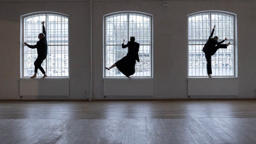Tre dansare står i varsitt stort fönster och gör rörelser.