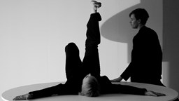 En dansare ligger på ett bord med ena benet uppsträckt. En person står bredvid.