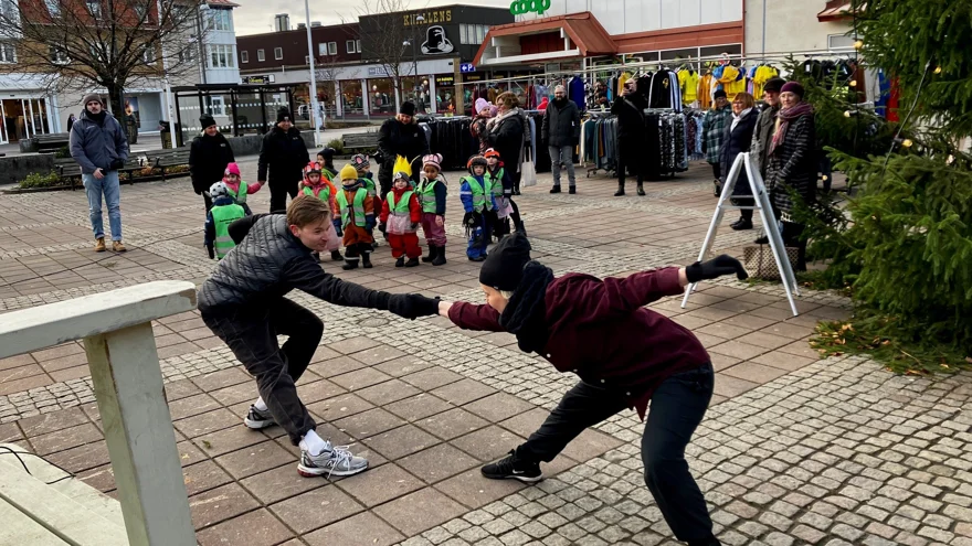 Två dansare håller varandras utsträckta händer framför en grupp med förskolebarn och andra vuxna.