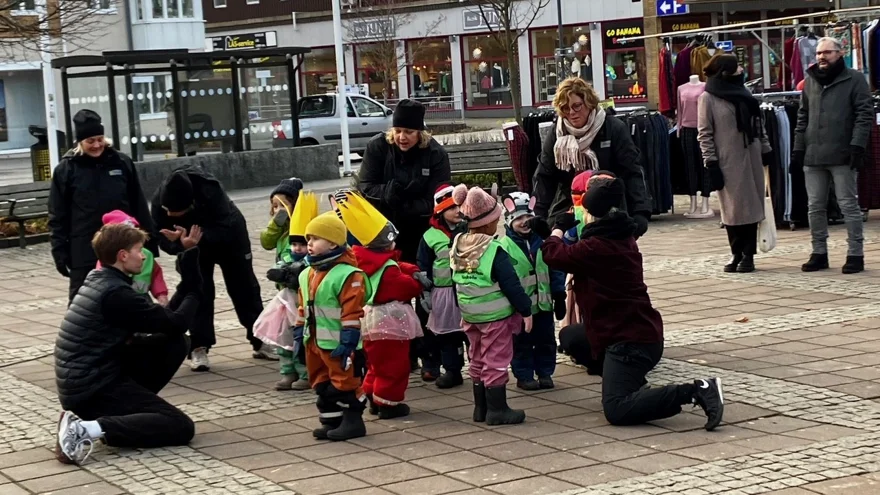 En grupp förskolebarn på ett torg med sina pedagoger och två dansare.