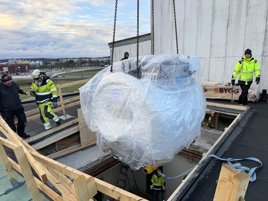 stor apparat lyfts ner genom ett hål i taket, under övervakning av ett antal personer.