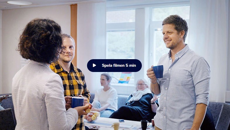 Tre personer samtalar över en kaffekopp. Några sitter i en soffa i bakgrunden.