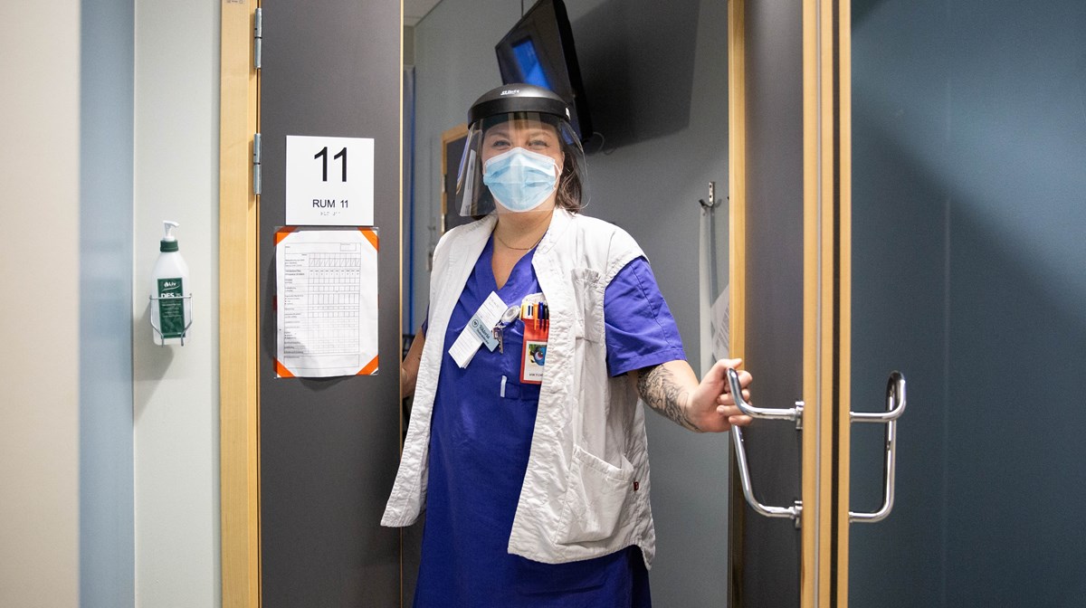 Kvinnlig vårdpersonal i skyddsutrustning öppnar en dörr