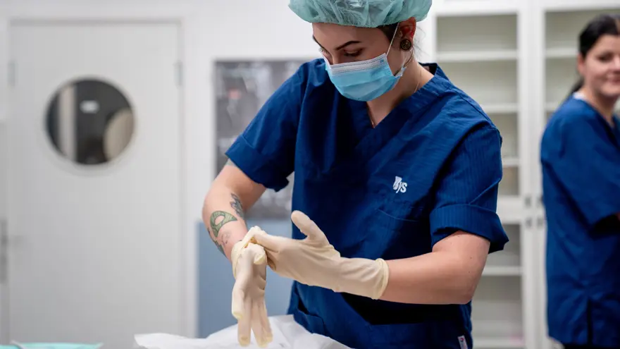 Djurvårdselev tar med skyddsmössa och munskydd tar på sig sterilhandskar