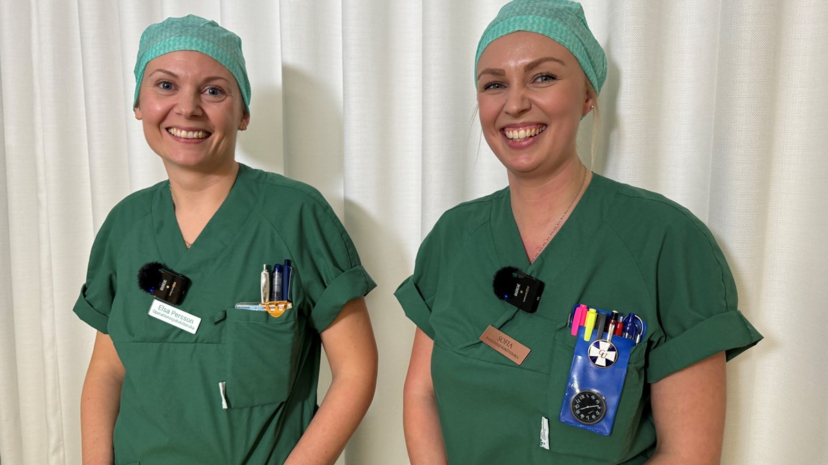Två grönklädda specialistsjuksköterskor har precis blivit filmade, mikrofonerna sitter kvar på deras sjukskötersekläder. De tittar in i kameran och ser väldigt glada ut.. 