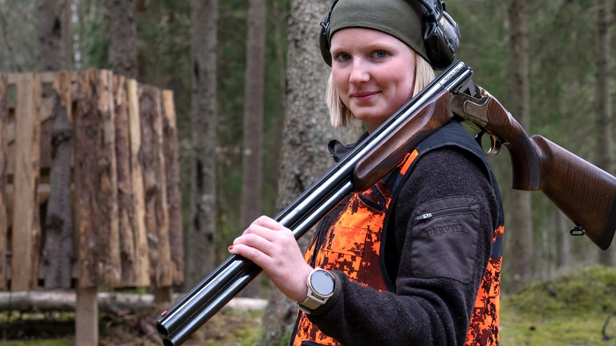  Hunting student with protective clothing and hearing protection stands with a rifle slung over her shoulder