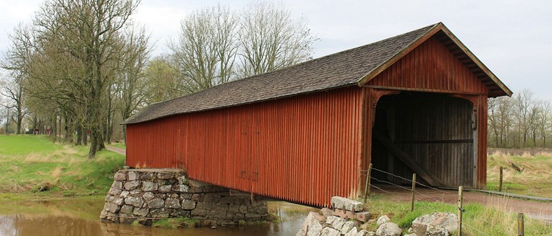 Vaholms övertäckta bro i Tidan. Byggnaden är av rött trä med mörkt tak.