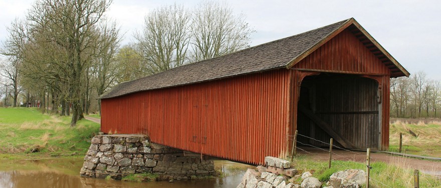 Vaholms övertäckta bro i Tidan. Byggnaden är av rött trä med mörkt tak.
