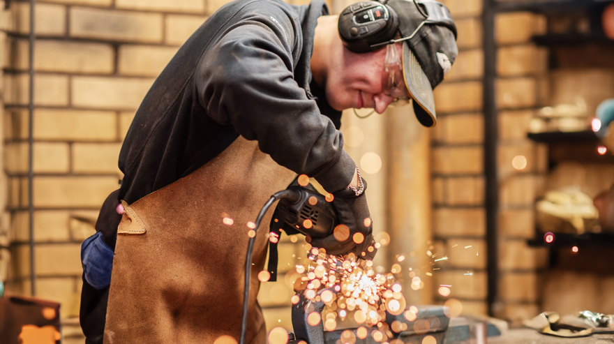 Elev med förkläde och hörselskydd kör vinkelslip