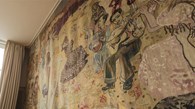 Foto visar en del av en stor etxtil som hänger på en vägg. Motivet är män som spelar på olika instrument och kvinnor som dansar.