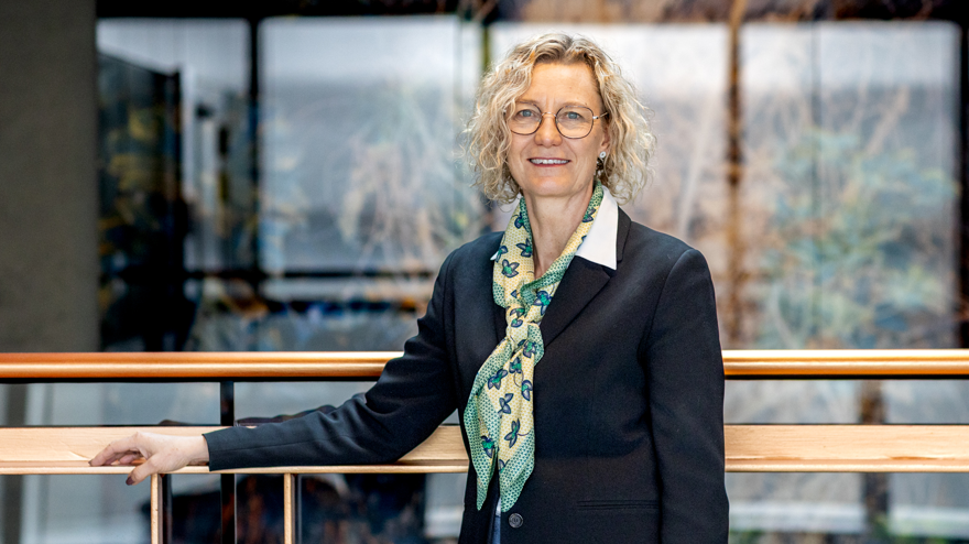 Kvinna i mörk kavaj och gulgrön scarf står med handen på ett räcke.