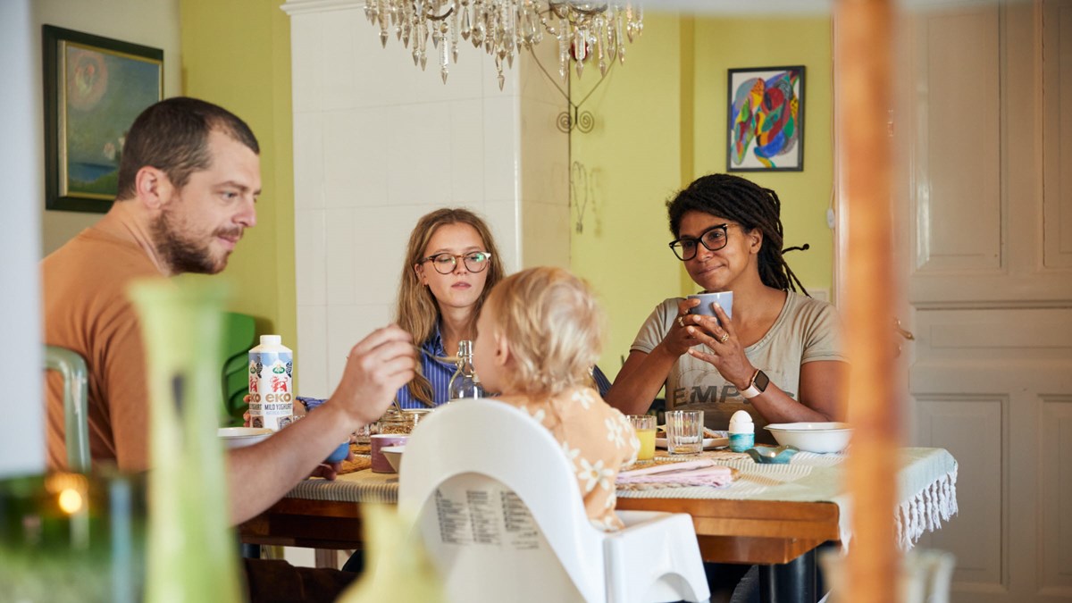 En familj med två vuxbna, en man o´ch en kvinna och två barn sitter vid ett bord äter frukost
