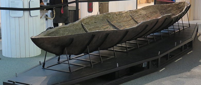 Bilden visar ett podium i en utställningslokal. På podiet står en mycket gammal stockbåt uppställd.